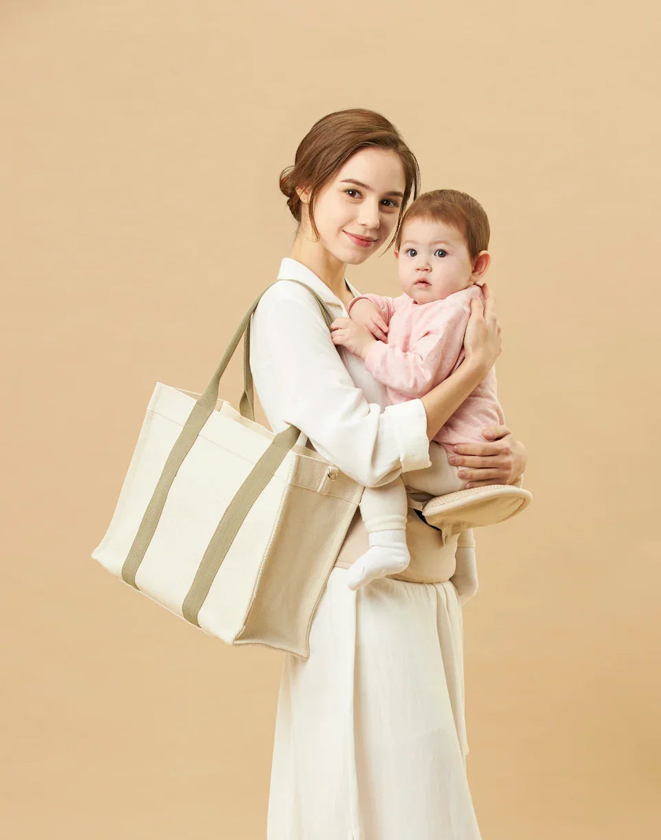 Mother carrying baby in ergonomic baby carrier, large tote bag, neutral background, bebefit.eu
